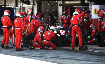 Ferrari pit crew in red uniforms surround a Formula 1 car during a pit stop with tires and equipment nearby