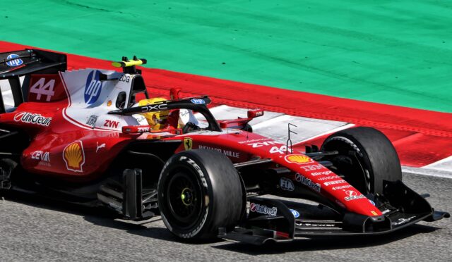 Red Ferrari Formula 1 car racing on the track with sponsor decals visible and green runoff area in the background.