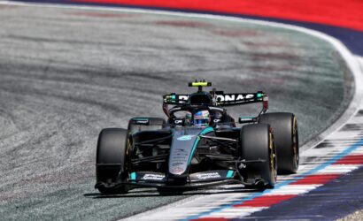Mercedes-AMG Petronas Formula One car speeding through a corner on a race track with red, white, and blue curbs.