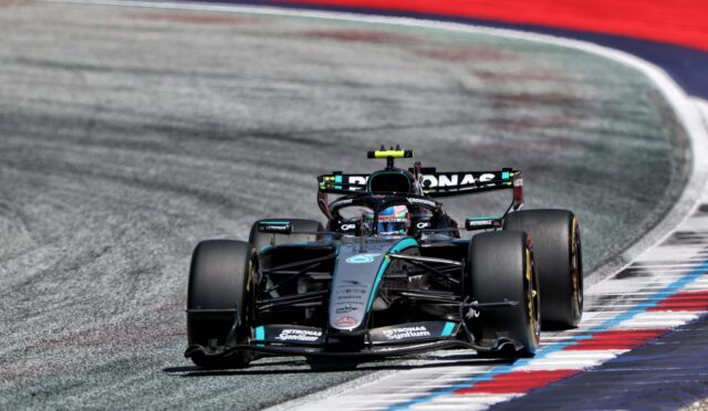 Mercedes-AMG Petronas Formula One car speeding through a corner on a race track with red, white, and blue curbs.