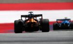 Rear view of an orange Formula 1 car on track, with Etihad branding on the rear wing and a second car blurred in the background.