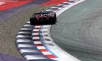 Red Formula 1 race car negotiating a sharp corner, hugging striped red, white, and blue curbs on the track.
