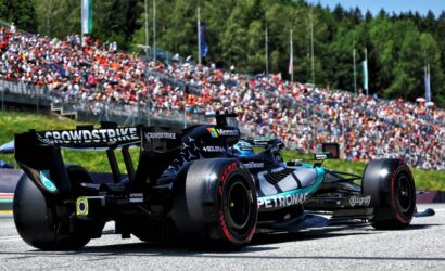 Race cars on track with a large crowd in the stands; close-up of a Formula 1 car featuring Petronas branding and a prominent rear wing reading 'CROWDSTRIKE'