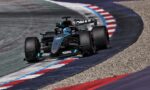Mercedes F1 racing car navigating a sharp left turn on a track with red, white, and blue curbs.