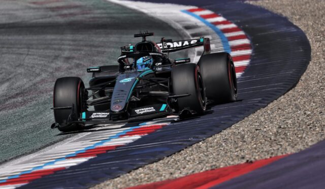 Mercedes F1 racing car navigating a sharp left turn on a track with red, white, and blue curbs.