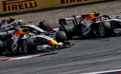 Formula 1 cars in a tight pack on a race track, with a large yellow Pirelli banner in the background.