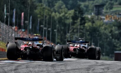 Three Formula 1 cars seen from behind speeding down a race track toward the camera with a blurred, forested backdrop behind them.