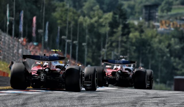 Three Formula 1 cars seen from behind speeding down a race track toward the camera with a blurred, forested backdrop behind them.