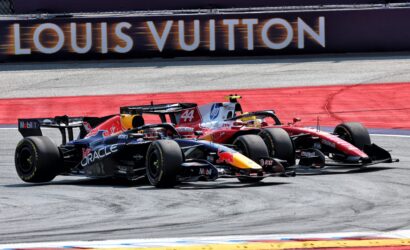 Two Formula 1 cars race side by side on a track, with a Louis Vuitton banner in the background, sponsor logos visible on the cars.