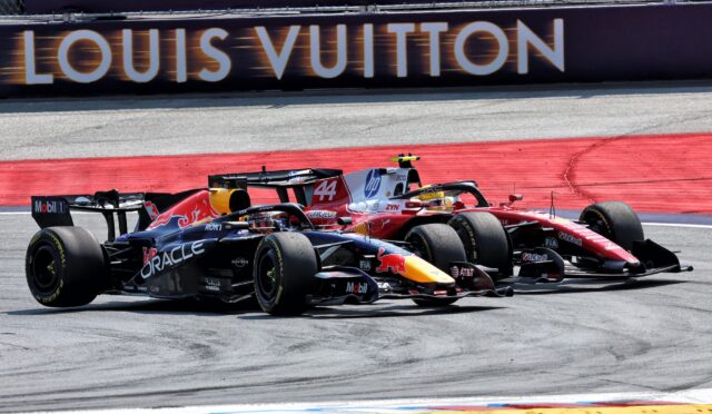Two Formula 1 cars race side by side on a track, with a Louis Vuitton banner in the background, sponsor logos visible on the cars.