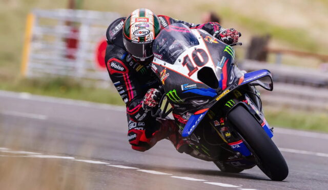 Race motorcycle rider leaning into a sharp left turn on a track, bike number 10 with sponsor logos visible.