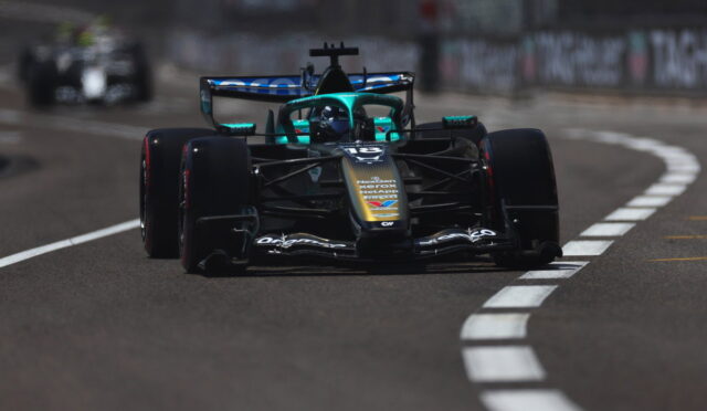 Front-facing Formula 1 car in black and turquoise, racing on a curved track with white dashed lines.