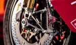 Close-up of a Brembo brake caliper and drilled rotor on a red sport motorcycle's front wheel.