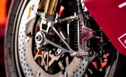 Close-up of a Brembo brake caliper and drilled rotor on a red sport motorcycle's front wheel.