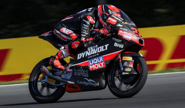 Rider in red‑black race suit leaning into a curve on a sponsor‑liveried racing motorcycle on a track, with DynamoLt and Liqui Moly logos visible.