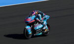 MotoGP rider on a blue race bike leaning into a turn on a dark asphalt track, number 80 visible on the front fairing