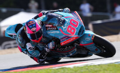 Motorcycle racer in teal-blue suit leaning into a sharp turn on a racetrack, bike number 68 with sponsor logos visible