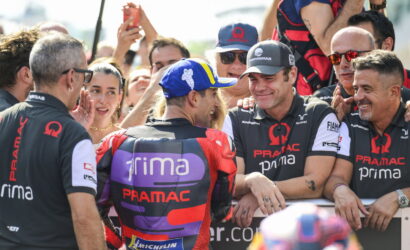Pramac Racing team members congratulate a rider in a colorful racing suit as fans cheer in the background.