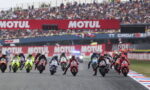 Motorcycle race start: riders in colorful suits accelerate from the grid as fans watch from grandstands under Motul banners.