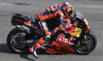 MotoGP rider in Red Bull KTM livery leaning into a left turn on a race track, mid-corner.