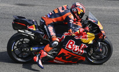 MotoGP rider in Red Bull KTM livery leaning into a left turn on a race track, mid-corner.