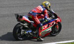 Professional motorcycle racer in a red, white, and blue suit leaning into a turn on a race track, helmeted and focused.