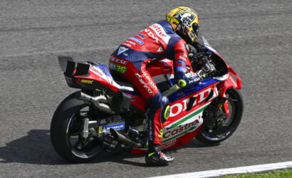 Professional motorcycle racer in a red, white, and blue suit leaning into a turn on a race track, helmeted and focused.