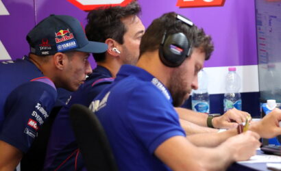 Three team members in blue uniforms wearing headsets lean over a desk, signing papers in a purple-branded room.