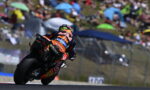 MotoGP rider in Red Bull livery leaning into a turn on a race track, with blurred spectators in the background