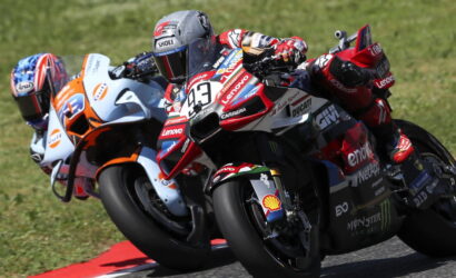 Four MotoGP riders lean into a turn on a race track with sponsor logos visible on the bikes and gear.