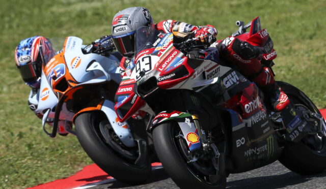 Four MotoGP riders lean into a turn on a race track with sponsor logos visible on the bikes and gear.