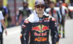 Racer in Red Bull KTM suit and cap with red-tinted glasses in a pit lane.