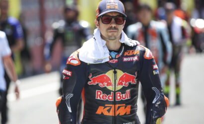 Racer in Red Bull KTM suit and cap with red-tinted glasses in a pit lane.