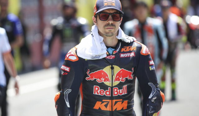 Racer in Red Bull KTM suit and cap with red-tinted glasses in a pit lane.