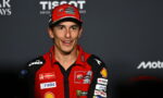 MotoGP rider in a red Ducati racing suit and cap, smiling at a media event.