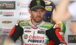 Racing rider in Castrol Power1 Honda suit sits in a pit area, wearing a black Monster cap and a focused expression amid sponsor banners behind him.” ,