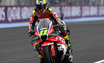 Motocross racer leaning into a turn on a red, white, and blue race bike number 11, wearing a neon-yellow and red suit and helmet on a race track.
