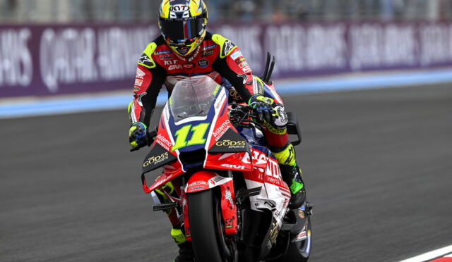 Motocross racer leaning into a turn on a red, white, and blue race bike number 11, wearing a neon-yellow and red suit and helmet on a race track.