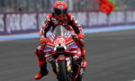 MotoGP rider in a red racing suit and helmet on a red race bike, number 93, covered in sponsor decals, on a race track