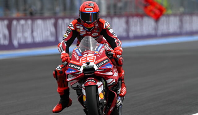 MotoGP rider in a red racing suit and helmet on a red race bike, number 93, covered in sponsor decals, on a race track