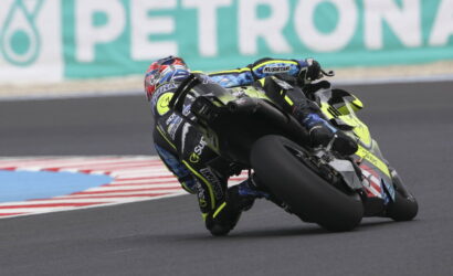 Motorcycle racer in blue-yellow leathers leans into a turn on a racetrack on a high-speed cornering moment with the bike tilted.