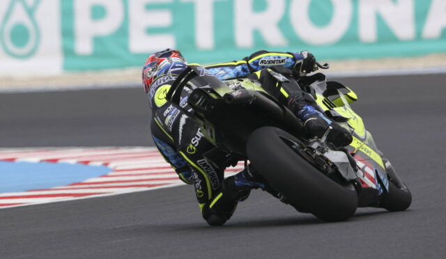 Motorcycle racer in blue-yellow leathers leans into a turn on a racetrack on a high-speed cornering moment with the bike tilted.