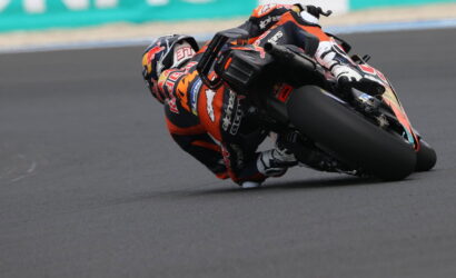 Motorcycle racer in orange and black gear leaning deeply into a turn on a race track