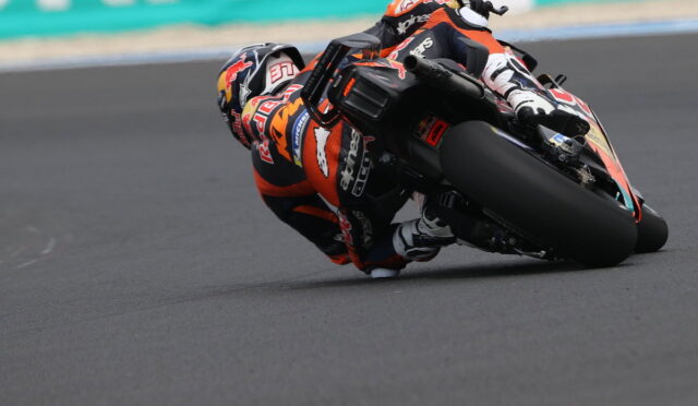 Motorcycle racer in orange and black gear leaning deeply into a turn on a race track