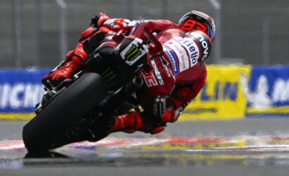 MotoGP rider in red gear leaning into a turn on a wet race track.