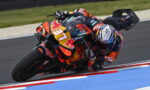 Motorcycle racer in colorful Red Bull livery leaning into a sharp turn on a race track, number 37 visible on the bike.