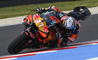 Motorcycle racer in colorful Red Bull livery leaning into a sharp turn on a race track, number 37 visible on the bike.