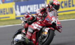Racing rider on a red Ducati motorcycle leaning into a corner with Lenovo and Monster Energy sponsorship visible on the bike and gear.