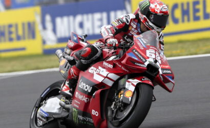 Racing rider on a red Ducati motorcycle leaning into a corner with Lenovo and Monster Energy sponsorship visible on the bike and gear.