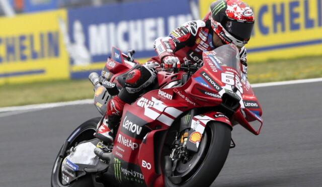Racing rider on a red Ducati motorcycle leaning into a corner with Lenovo and Monster Energy sponsorship visible on the bike and gear.